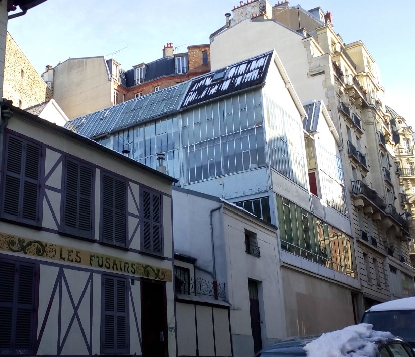 A view of the artists studios Cité des fusains from the Rue tourlaque Paris 75018. There is some snow on the cars in the foreground and on the glass studios.