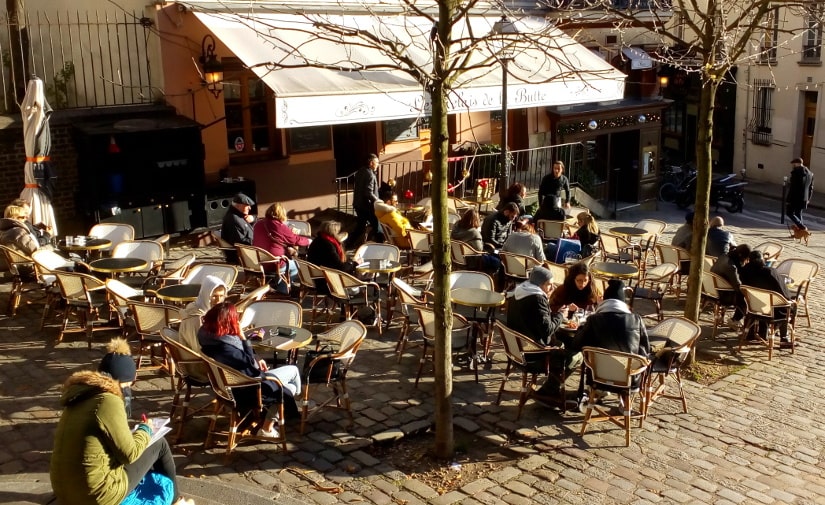 People sitting on a terrace at a cafe in a quiet square in Montmartre Paris. An artist draws the scene from some steps leading from square