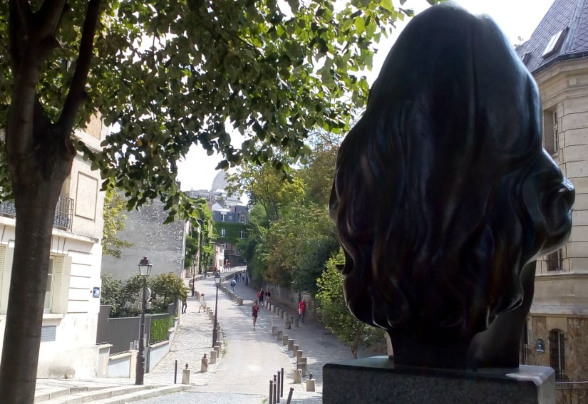 A view of the winding Rue de l’Abreuvoir Montmartre with in the foreground the back of the bust of the French singer Dalida in Place Dalida Montmartre.