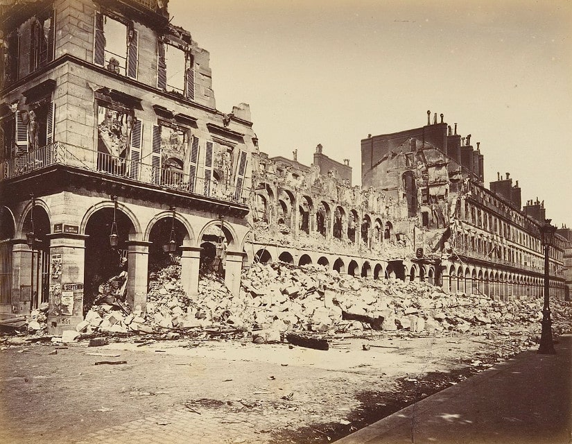 Black and White contemporary photograph by Alphonse J Liébert of the damage on Rue de Rivoli. The photograph shows destroyed and partially destroyed buildings with the fallen debris on Rue de Rivoli. The debris reaches to the top of the Rue de Rivoli arches.