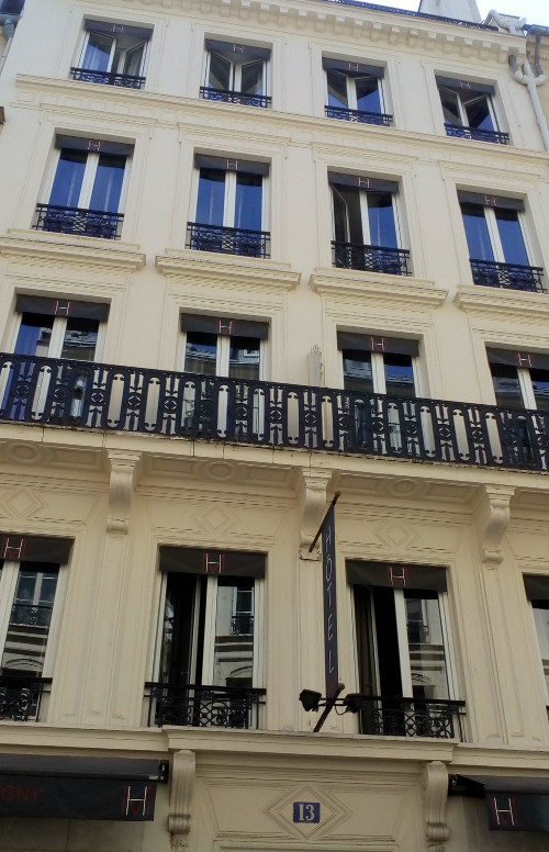 A view of a white painted four storey hotel facade at 13 Rue Victor Massé Montmartre. A wrought iron balcony and cornice runs across the facade on the second floor. The building is now a hotel but used to be Degas’ apartment and studio in the 1860s.