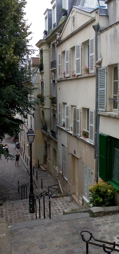 Steps leading to the narrow Rue André Antoine Montmartre Paris 75018. White buildings, a gas lamp, balconies, shutters and window plants. The building in the foreground is Georges Seurat’s last studio in Montmartre.
