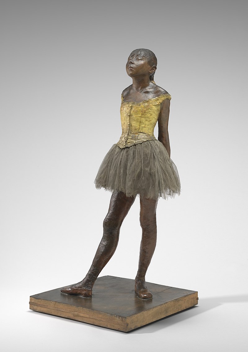 A bronze statuette of a ballet dancer assuming a rigid and contorted ballet pose. She wears a tutu, bodice and ballet shoes, she has real hair. Her face is upturned with a hint of defiance and pride in her expression.