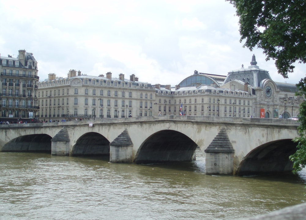 The Pont Royal bridge in Paris which links the Louvre Museum site to the nearby Orsay Museum. The stone arches of the bridge span the Seine. The nearby Orsay Museum is visible behind the bridge in this view looking south-west.
